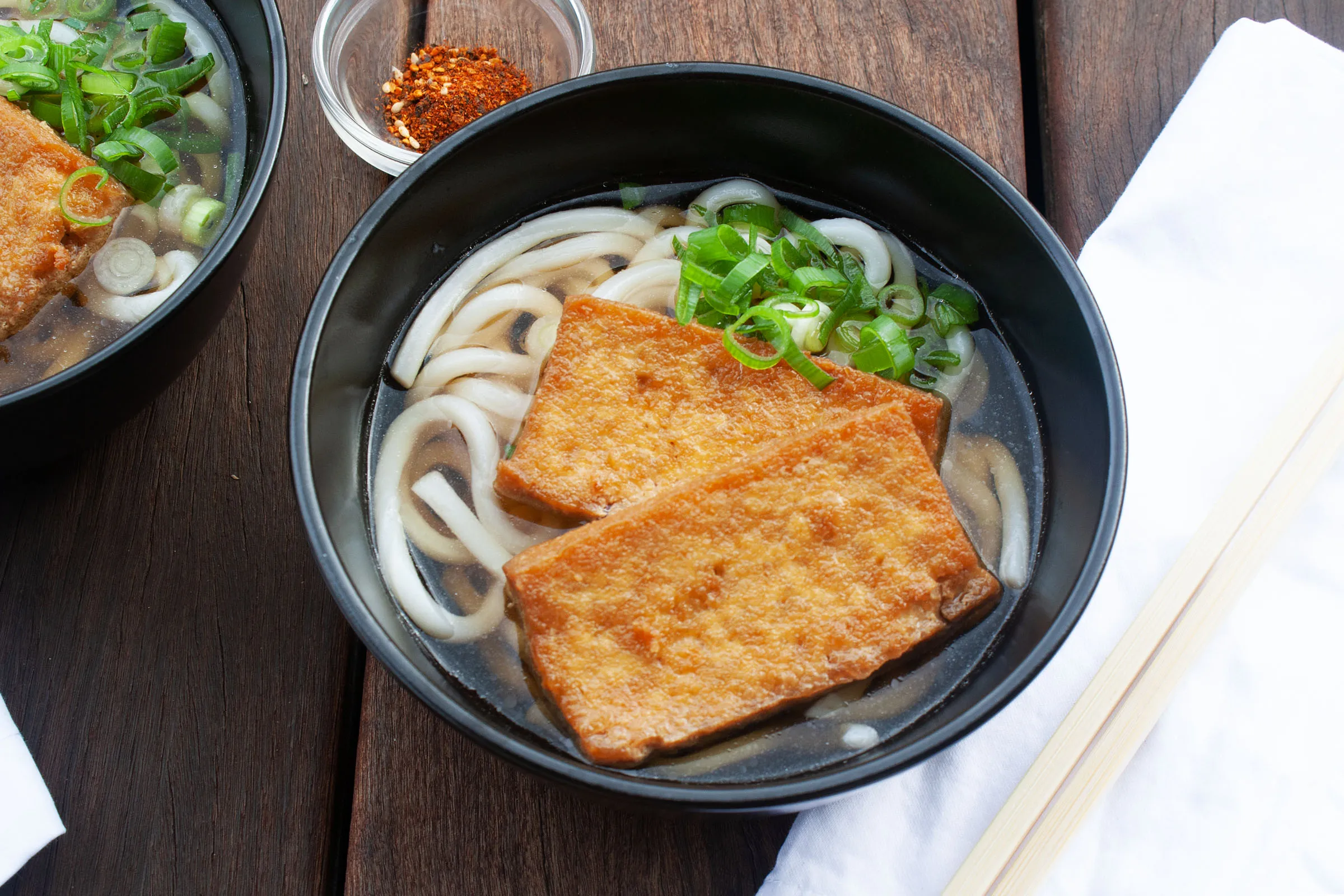 Steaming bowls of comfort noodle dishes including udon, ramen, and tempura arranged on a wooden table